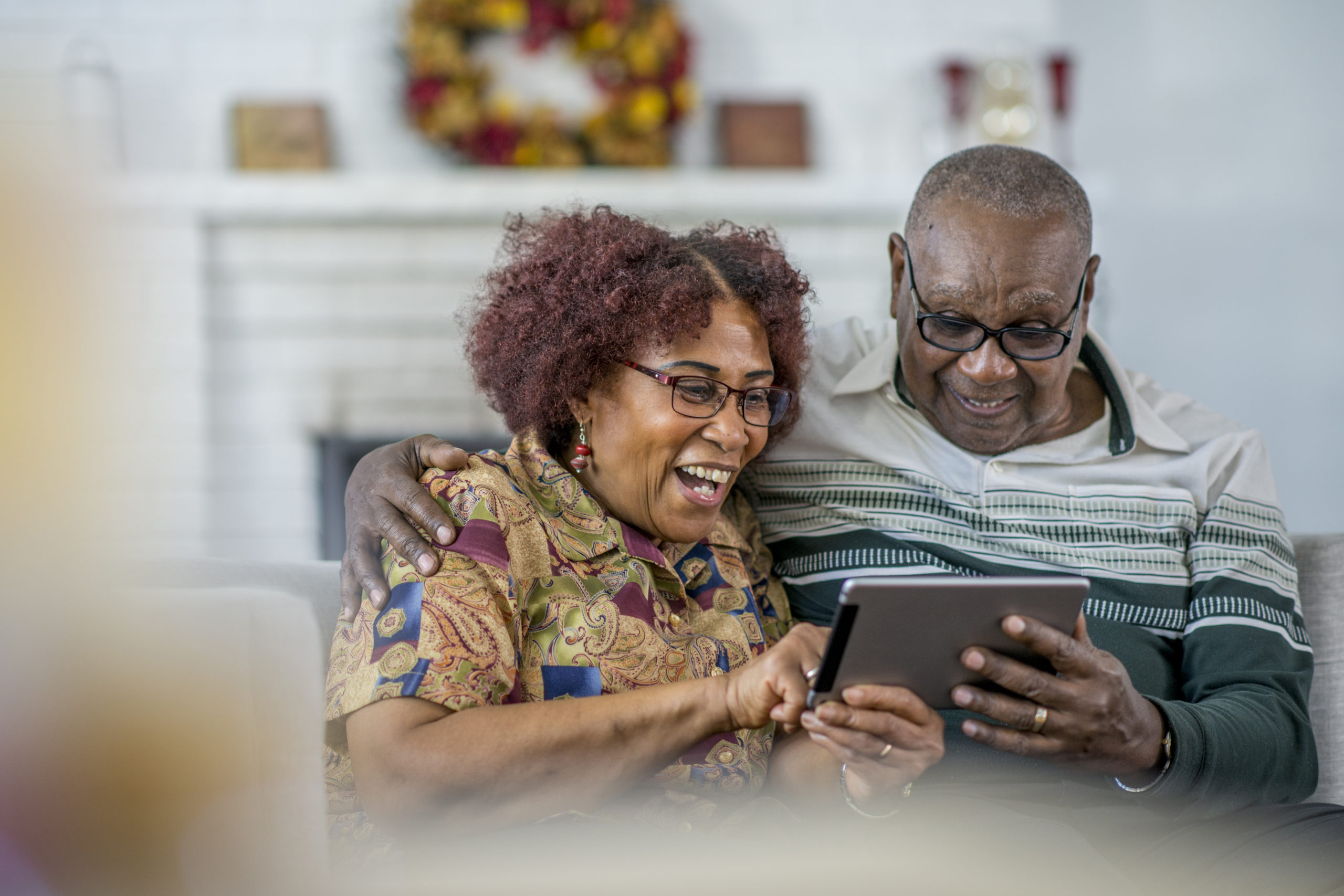 A senior couple of African descent sitting on a couch in their living room watching on their tablet